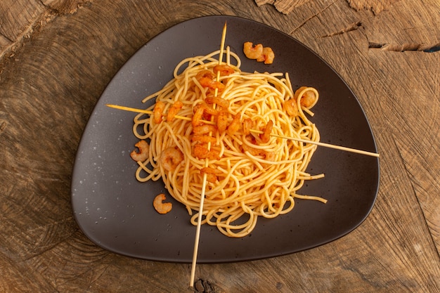 Top view of cooked italian pasta with shrimps inside brown plate on the wooden surface