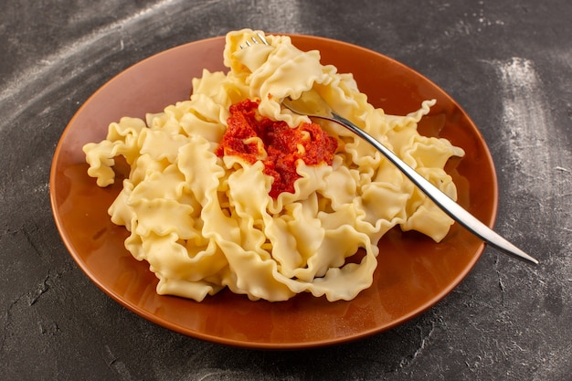 A top view cooked italian pasta with tomato sauce inside brown plate