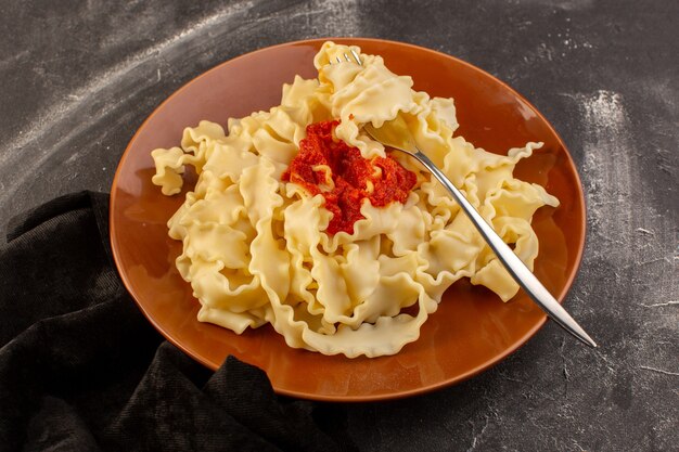 A top view cooked italian pasta with tomato sauce inside plate on the grey table food meal italian pasta dish