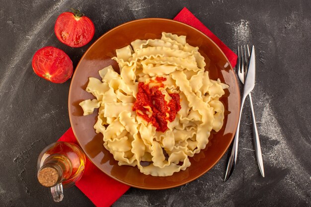 A top view cooked italian pasta with tomato sauce inside plate with cutlery and tomatoes