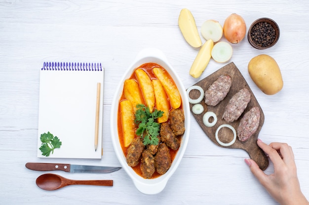 Вид сверху приготовленных мясных котлет с соусом из картофеля и зелени вместе с сырым мясом на светлом столе, еда, мясо, овощ