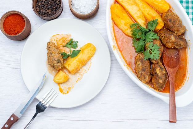 Top view of cooked meat cutlets with spicy sauce potatoes and green seasonings on light desk, food meal meat vegetable