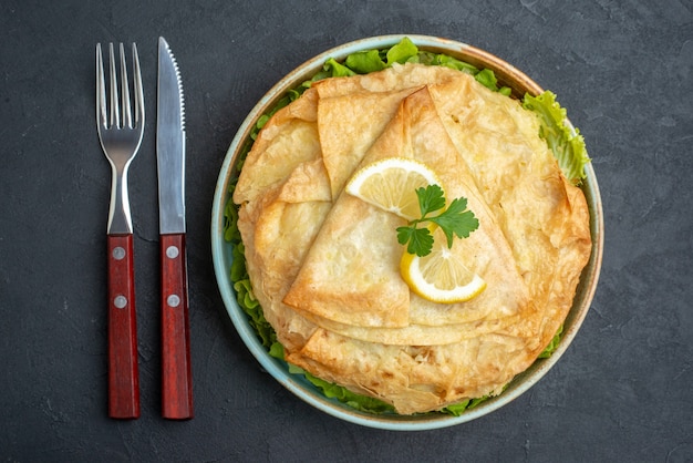 Top view cooked pita inside plate with greens and lemon slices on dark surface