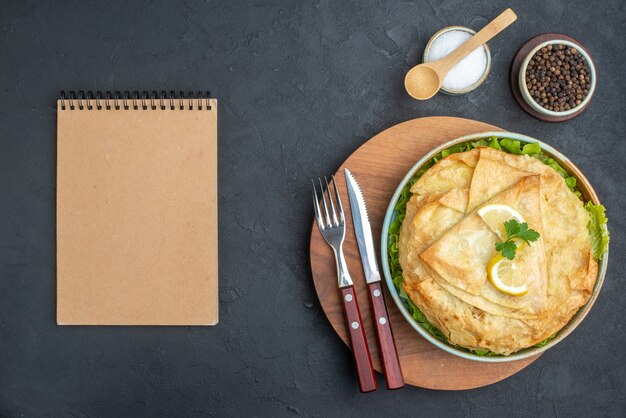 Top view cooked pita inside plate with greens and lemon slices on dark surface