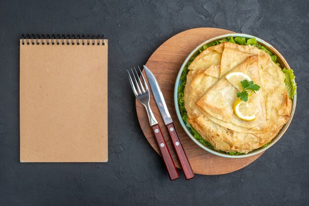 Top view cooked pita inside plate with greens and lemon slices on dark surface