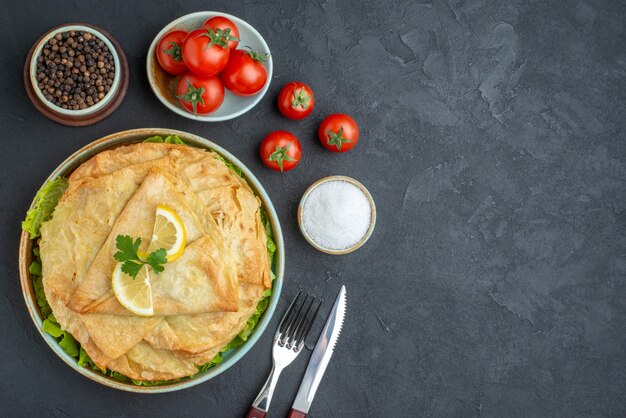 Top view cooked pita inside plate with lemon slices and cutlery on dark surface