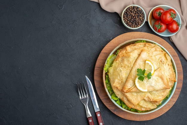 Top view cooked pita inside plate with lemon slices and cutlery on dark surface