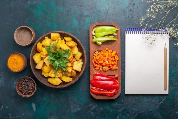 Top view cooked potatoes with greens along with seasonings and sliced peppers on dark blue surface