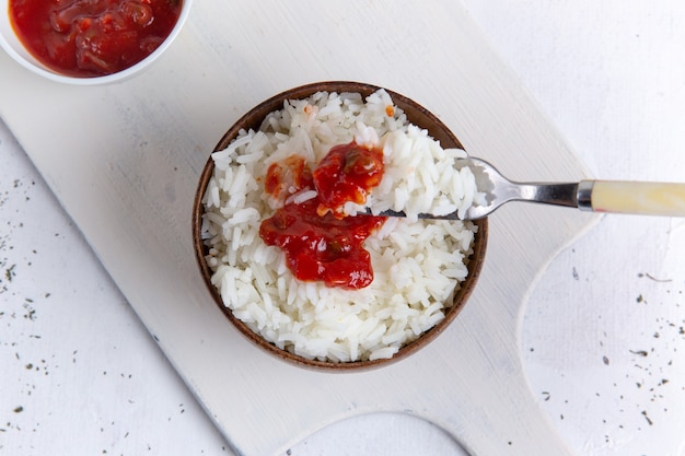 Top view of cooked rice tasty meal inside brown pot with red spicy sauce on white surface