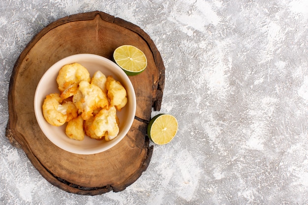 Top view of cooked sliced cauliflower inside plate with lemon on grey-light surface