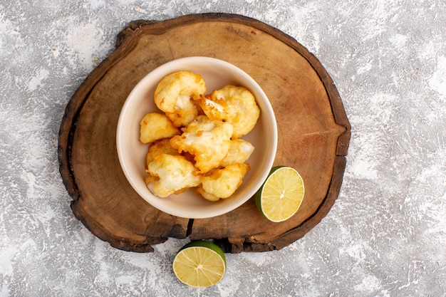 Top view of cooked sliced cauliflower inside plate with lemon on the grey-light surface