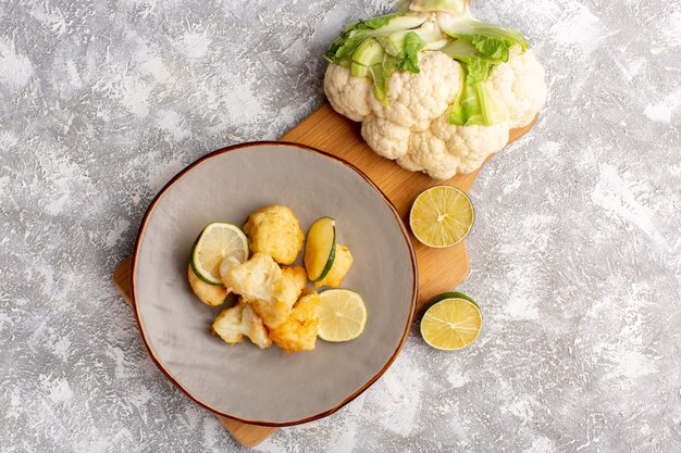 Top view of cooked sliced cauliflower inside plate with lemon on white surface