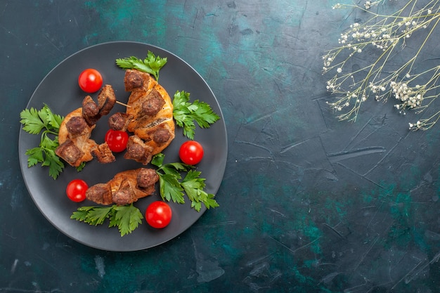 Бесплатное фото Вид сверху приготовленное нарезанное мясо с зеленью и красными помидорами черри на темно-синем столе