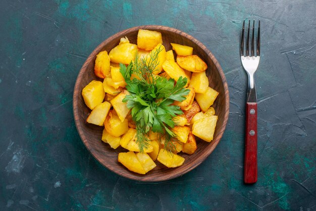 Top view cooked sliced potatoes delicious meal with greens inside brown plate on dark-blue desk