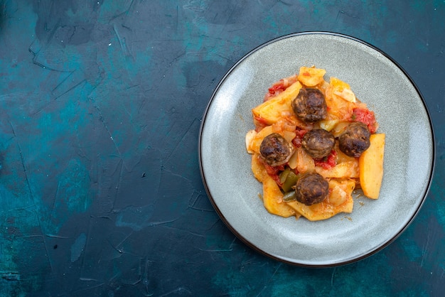 Top view cooked sliced potatoes with meatballs inside plate on dark blue background.