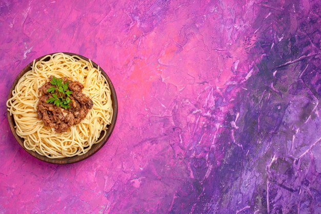 Вид сверху приготовленные спагетти с мясным фаршем на розовом столе, тесто, блюдо из макарон