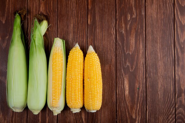 Top view of cooked and uncooked corn cobs on left side and wood with copy space