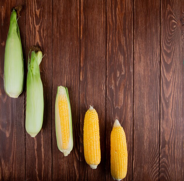 Top view of cooked and uncooked corn cobs on left side and wood with copy space