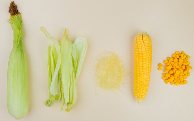 Вид сверху приготовленной сырой кукурузы с вареными зернами кукурузной скорлупы и кукурузного шелка на белой поверхности