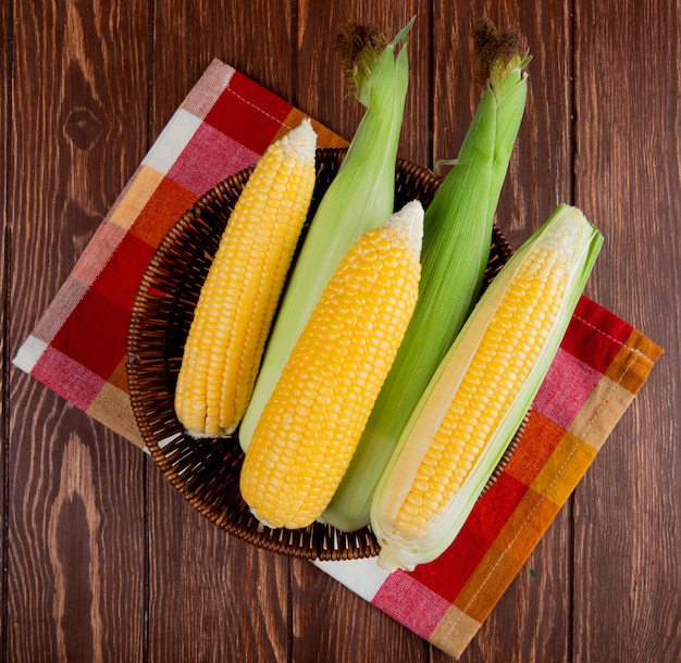 Free photo top view of cooked and uncooked corns in basket on cloth and wooden surface