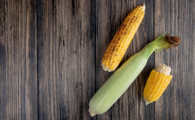 Free photo top view of cooked and uncooked corns on right side and wooden surface with copy space