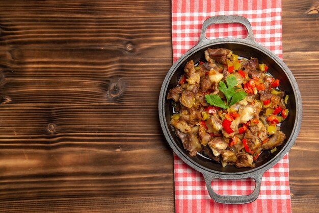 Top view cooked vegetable meal including vegetables and meat inside on the wooden brown desk