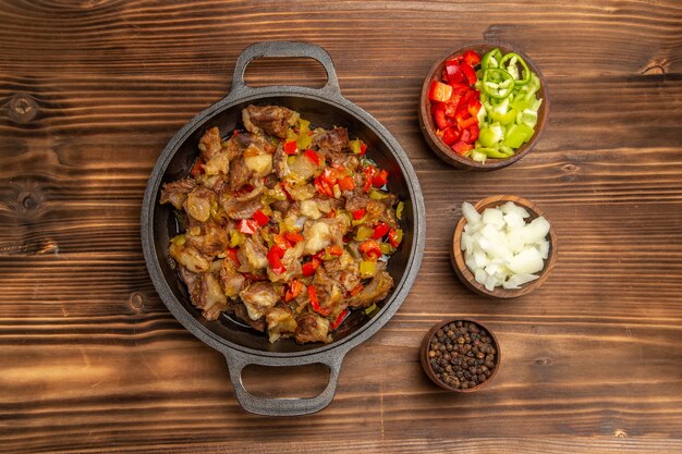 Top view cooked vegetable meal with meat and fresh sliced bell-pepper on the wooden brown desk