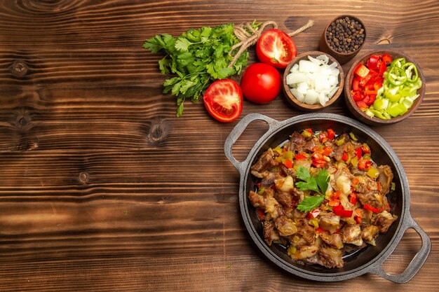 Top view cooked vegetable meal with meat and greens on the wooden brown desk