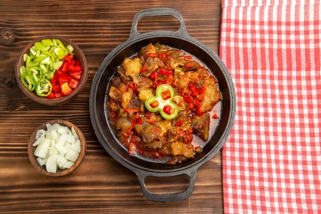Вид сверху приготовленной овощной еды с мясом и нарезанным болгарским перцем на коричневой деревянной поверхности