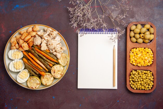 Top view cooked vegetables with egg meal beans and notepad on dark space