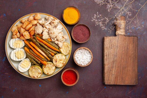 Top view cooked vegetables with egg meal and seasonings on dark desk