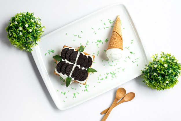 葉と白い背景の甘い夏の菓子の白い机の中のアイスクリームで飾られたチョコレートビスケットカスタードとトップビュークッキーデザート