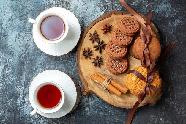 Top view cookies and biscuits anises cinnamon sticks on round wood board two cups of tea on dark table