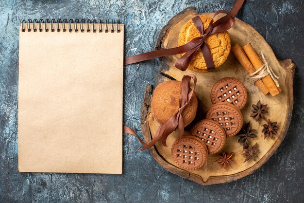 Top view cookies and biscuits anises cinnamon sticks tied with rope on wood board notepad on dark table