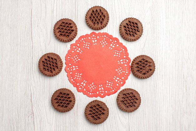 Top view cookies and the red oval lace doily on the white wooden table