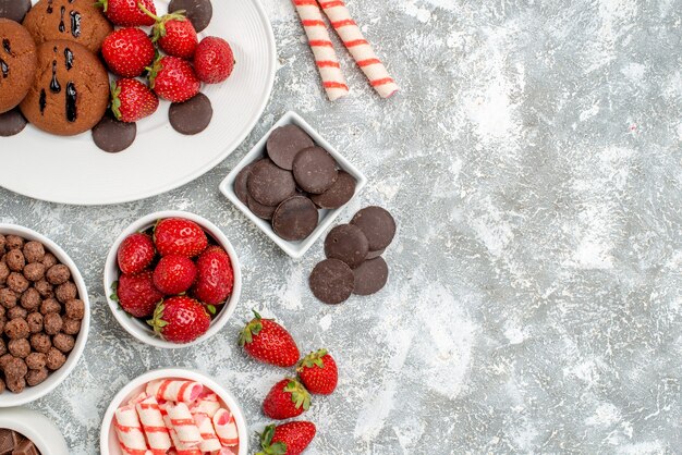 회색-흰색 테이블의 왼쪽에 사탕 딸기 초콜릿 시리얼과 타원형 접시 그릇에 상위 뷰 쿠키 딸기와 둥근 초콜릿