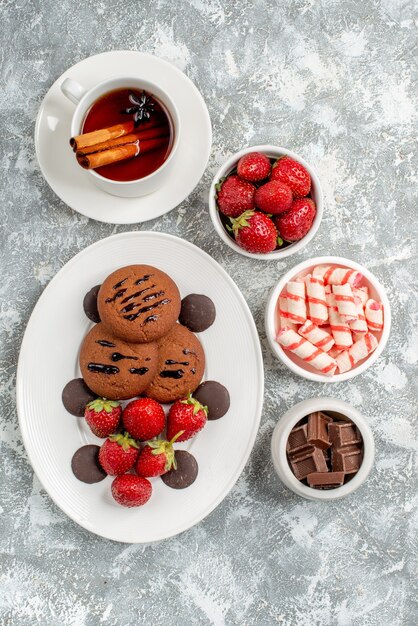 사탕의 그릇으로 둥근 타원형 접시에 상위 뷰 쿠키 딸기와 둥근 초콜릿 딸기 초콜릿 계피 티온 회색 흰색 테이블