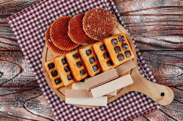 Top view cookies and waffles on cutting board on cloth and wooden background. horizontal