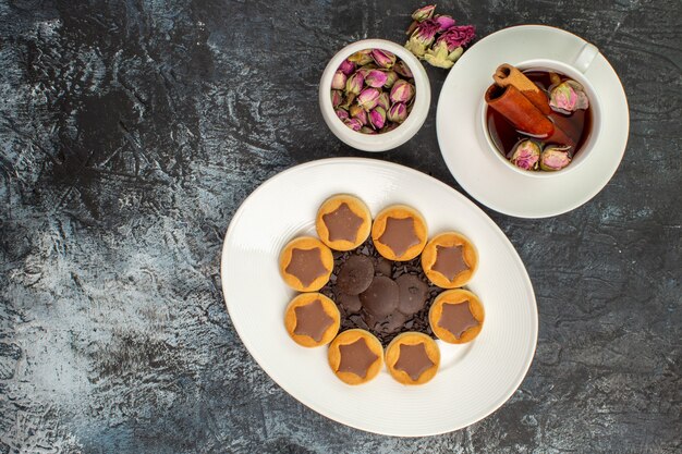 Top view of cookies on white plate with a cup of herbal tea with a bowl of dry flower on grey ground