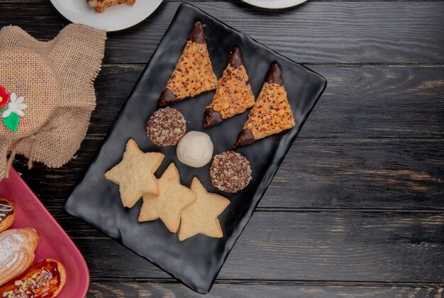 Top view of cookies with cake slices in plate and cakes on wooden background with copy space