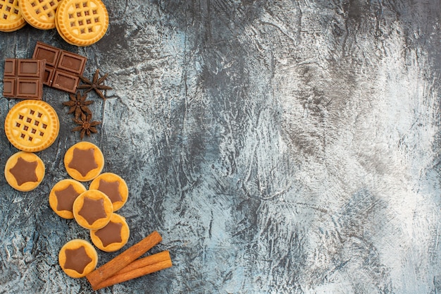 Top view of cookies with cinnamon sticks and chocolates on the left side of grey ground