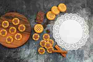 Foto gratuita vista dall'alto di biscotti sul piatto di legno e pizzo bianco con cannella e cioccolato su sfondo grigio
