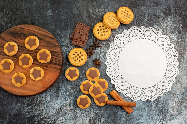 Top view of cookies on wooden platter and white lace with cinnamon and chocolate on grey background