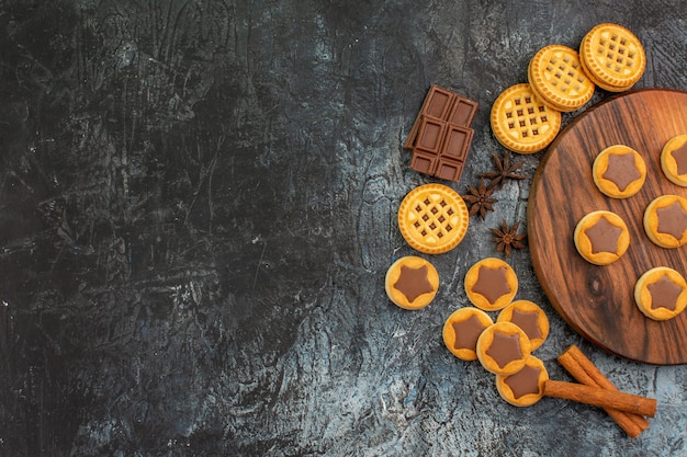 Top view of cookies on wooden platter with anise and chocolate and cinnamons on grey background