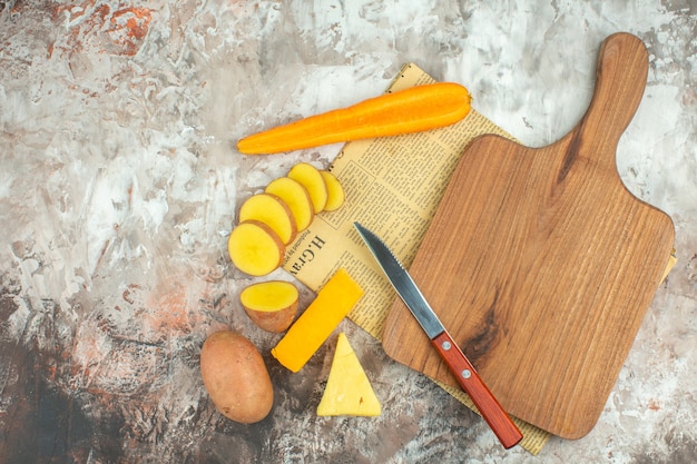 Top view of cooking background with various vegetables and two kinds of cheese knife and wooden cutting board on an old newspaper on mixed color background