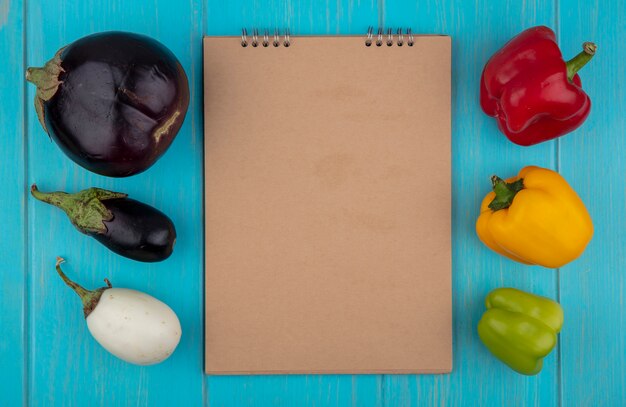 Top view  copy space beige notepad with colored bell peppers and eggplants on turquoise background