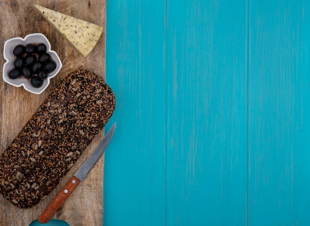 Top view  copy space black bread on a stand with cheese  olives in a bowl on a turquoise background