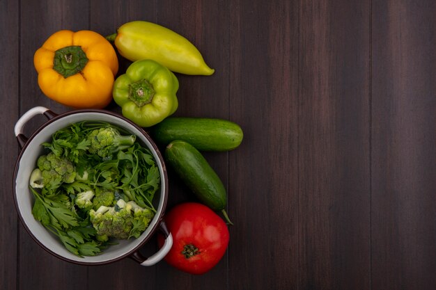 Top view  copy space broccoli in a saucepan with parsley and cucumbers and peppers on wooden background