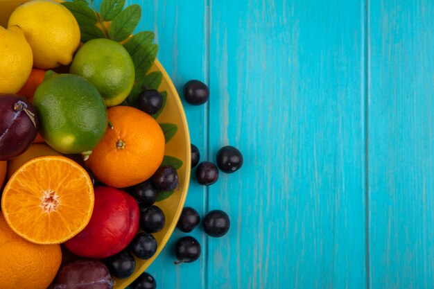 Top view  copy space cherry plum with oranges  plums  lemons and limes on a yellow plate  on a turquoise background