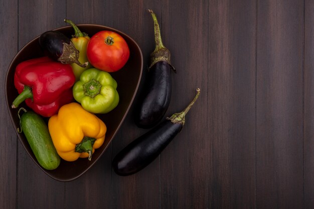 Top view  copy space colored bell peppers with cucumbers and tomatoes in bowl with eggplant on wooden background